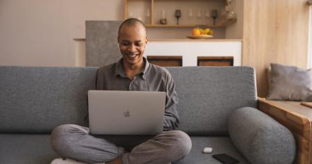 A man sitting on a couch in a living room on his laptop working from home and using Splashtop Enterprise